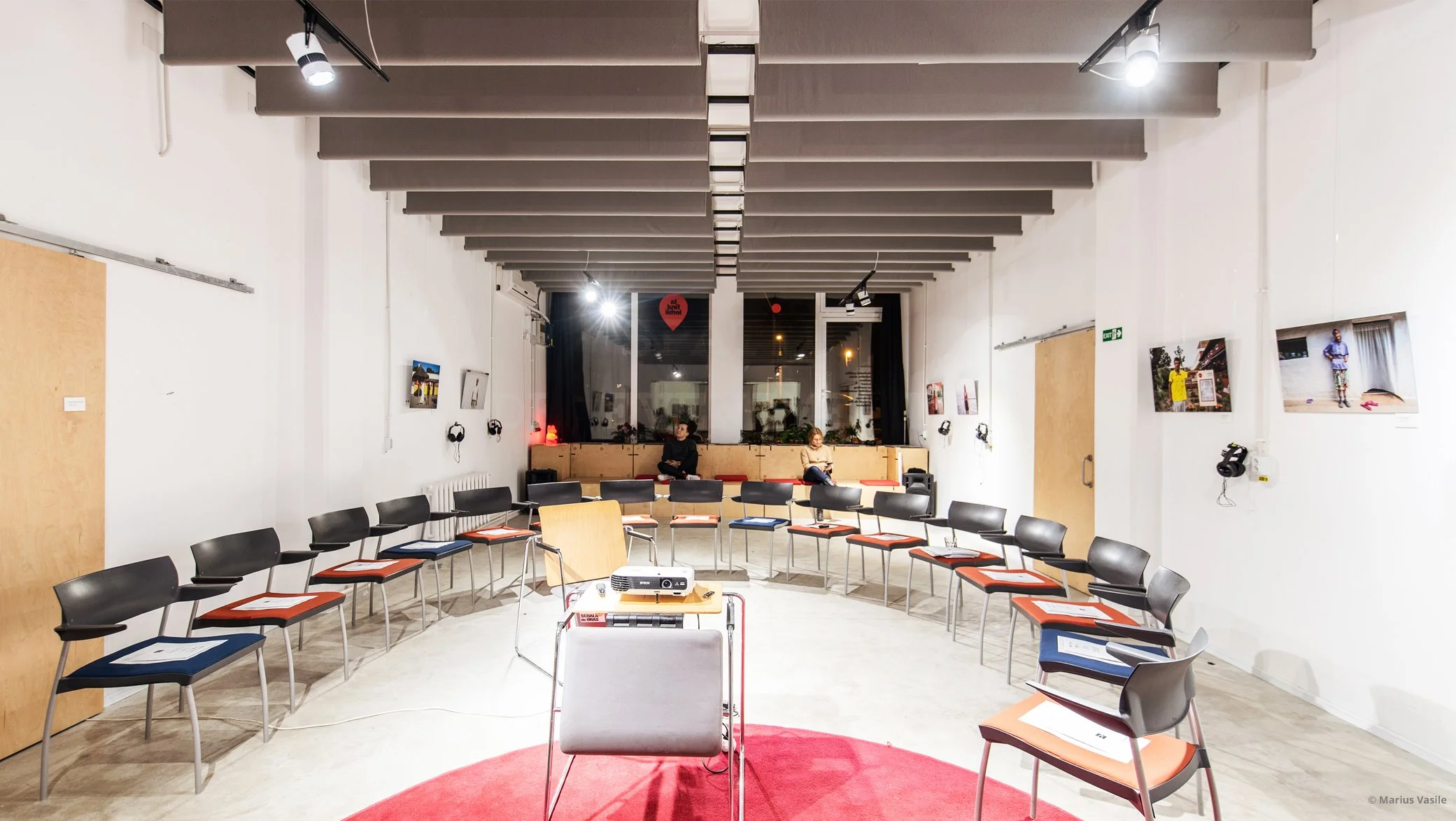 Sala mare de La Firul Ierbii în care sunt dispuse scaune în cerc. În mijloc un proiector, iar pe structurile din spate doi oameni care așteaptă începerea unui eveniment
