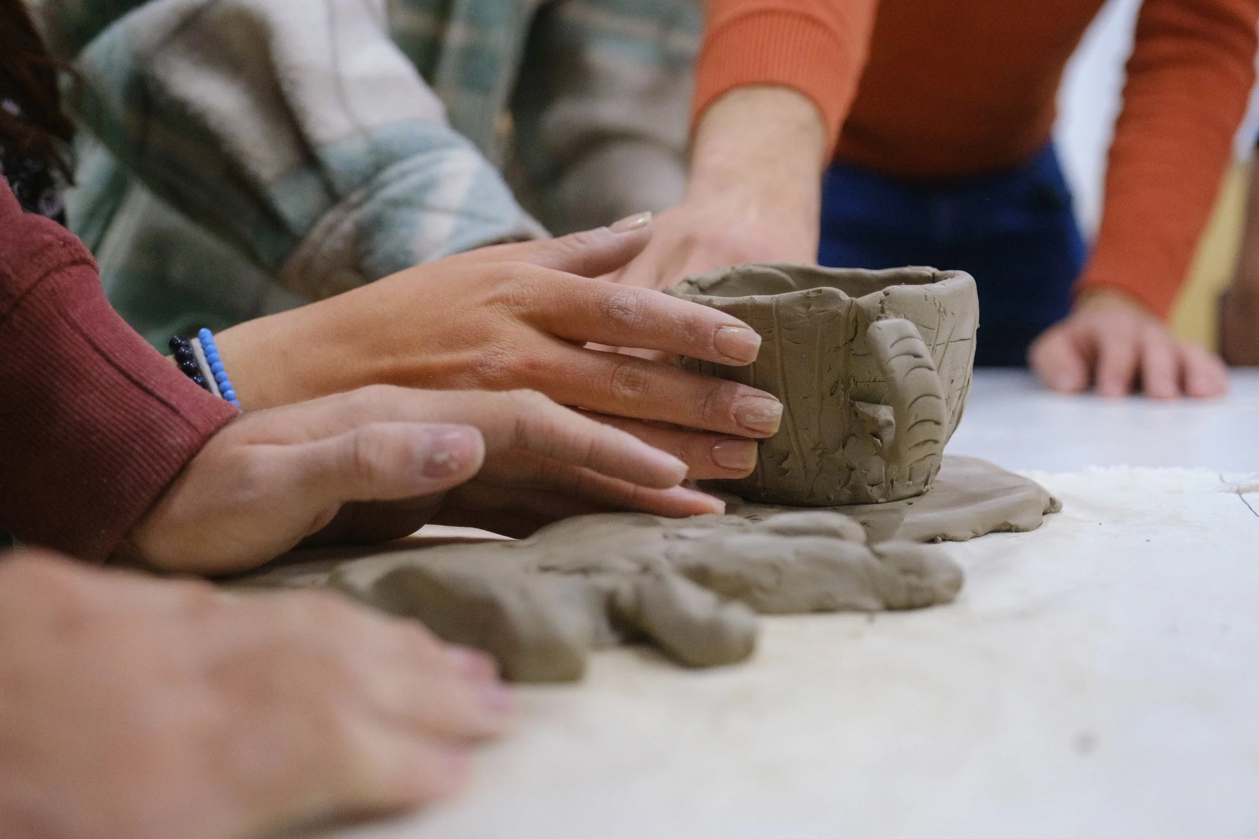 Două mâini modelează o cană din ceramică