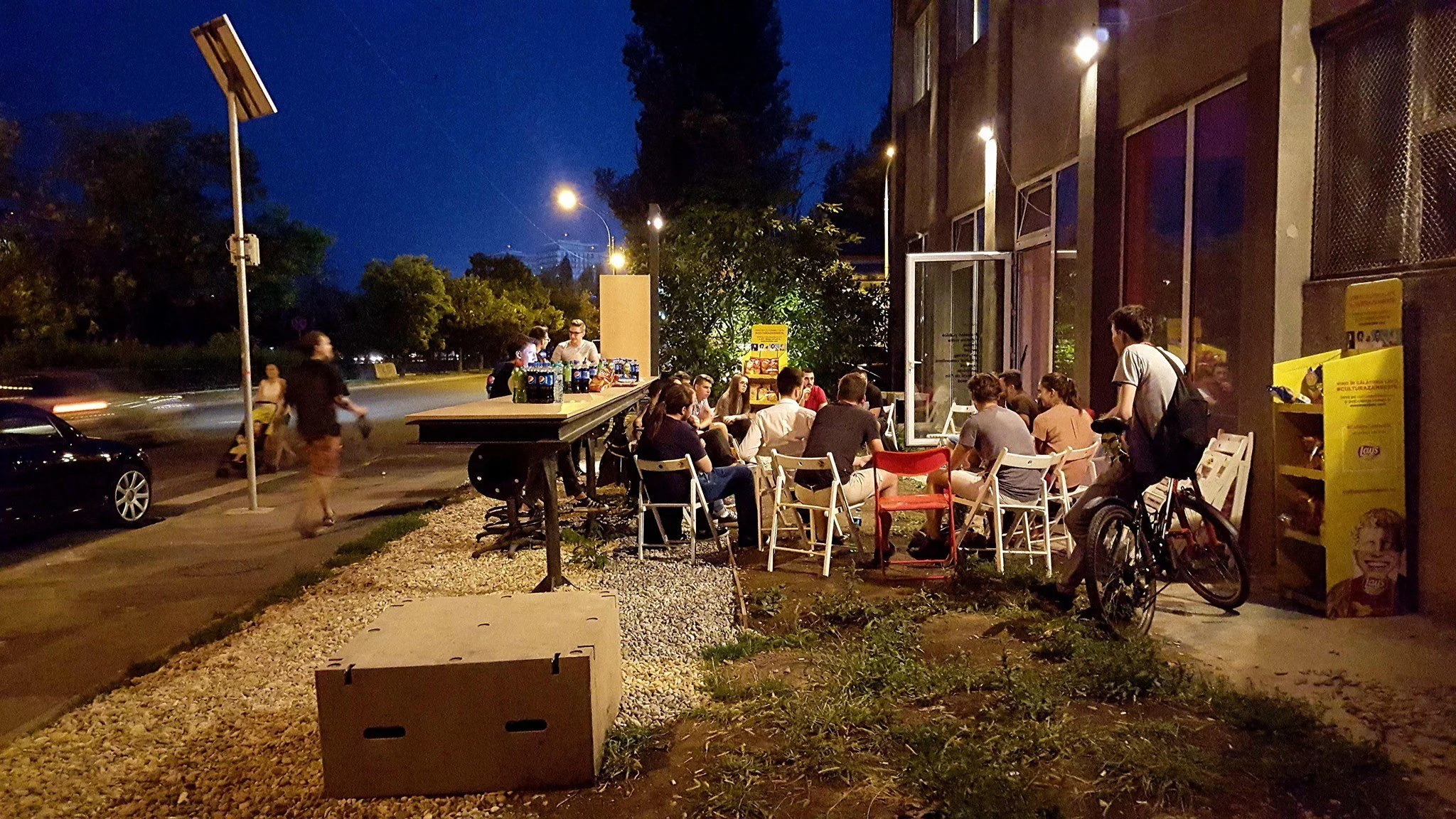 Mai multe persoane stau în grădina La Firul Ierbii. Imaginea este surprinsă seara