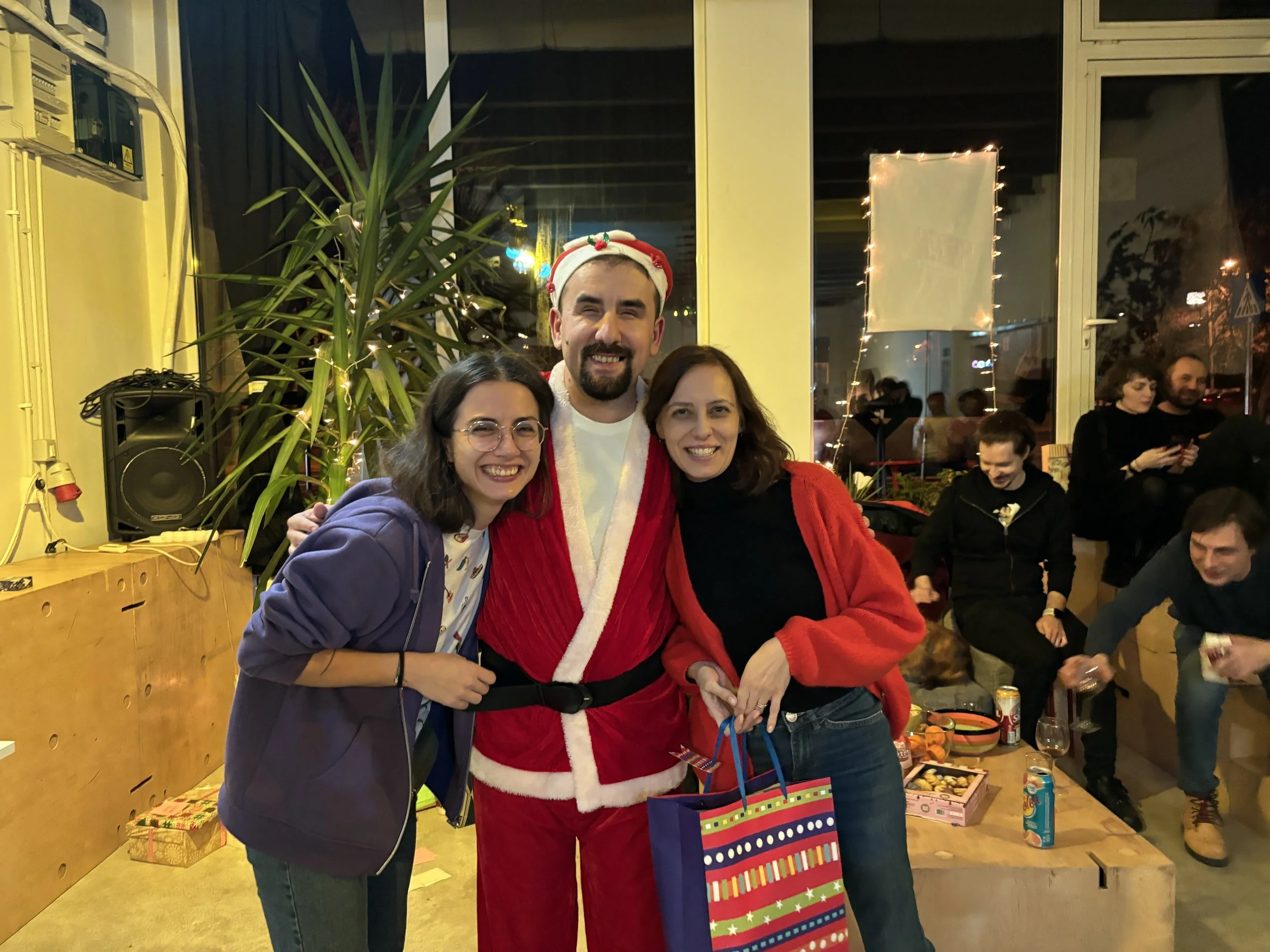 Două fete stau la poză alături de un bărbat îmbrăcat în Moș Crăciun. Imaginea este surprinsă în timpul petrecerii de Crăciun de La Firul Ierbii