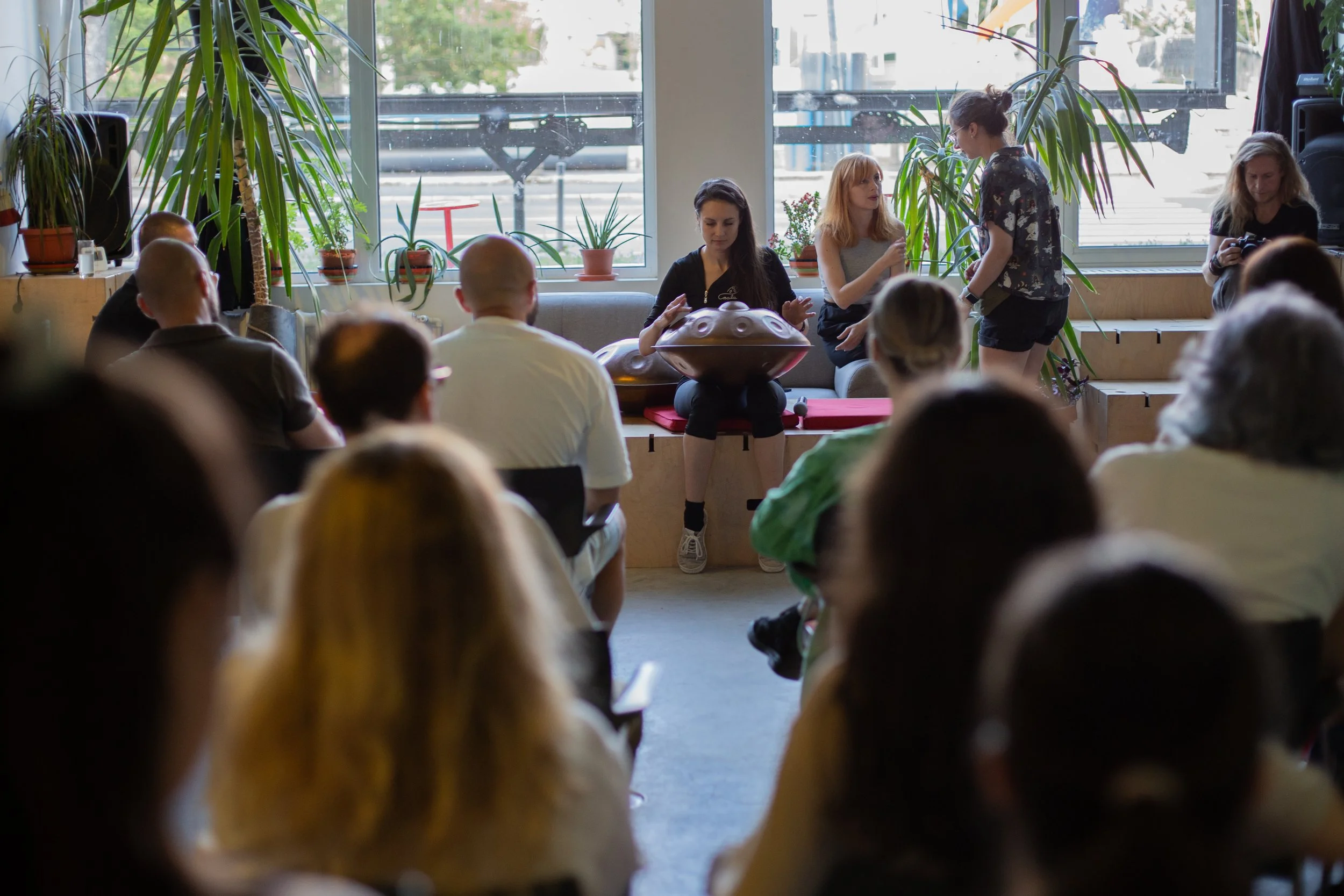 Imaginea este surprinsă în timpul concertului atelier de handpan susținut de Nala Sound Sculptures. Mai multe persoane o privesc pe Roxana Raluca Iancu în timp ce cântă la instrument în sala mare de La Firul Ierbii