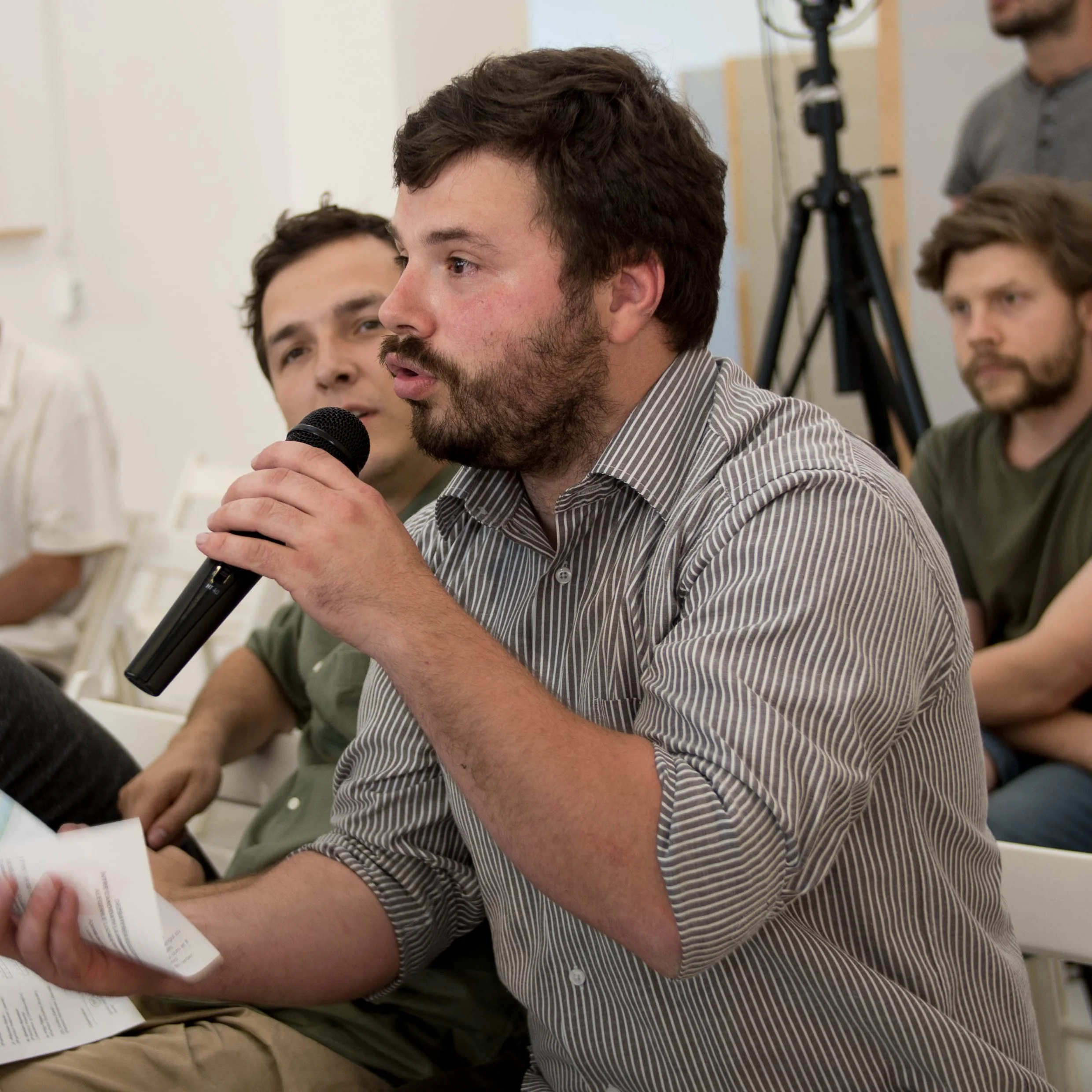 În imagine este Iulian Canov, unul dintre fondatorii La Firul Ierbii în timpul unei dezbateri. El ține în mână un microfon și este surprins în timp ce discută