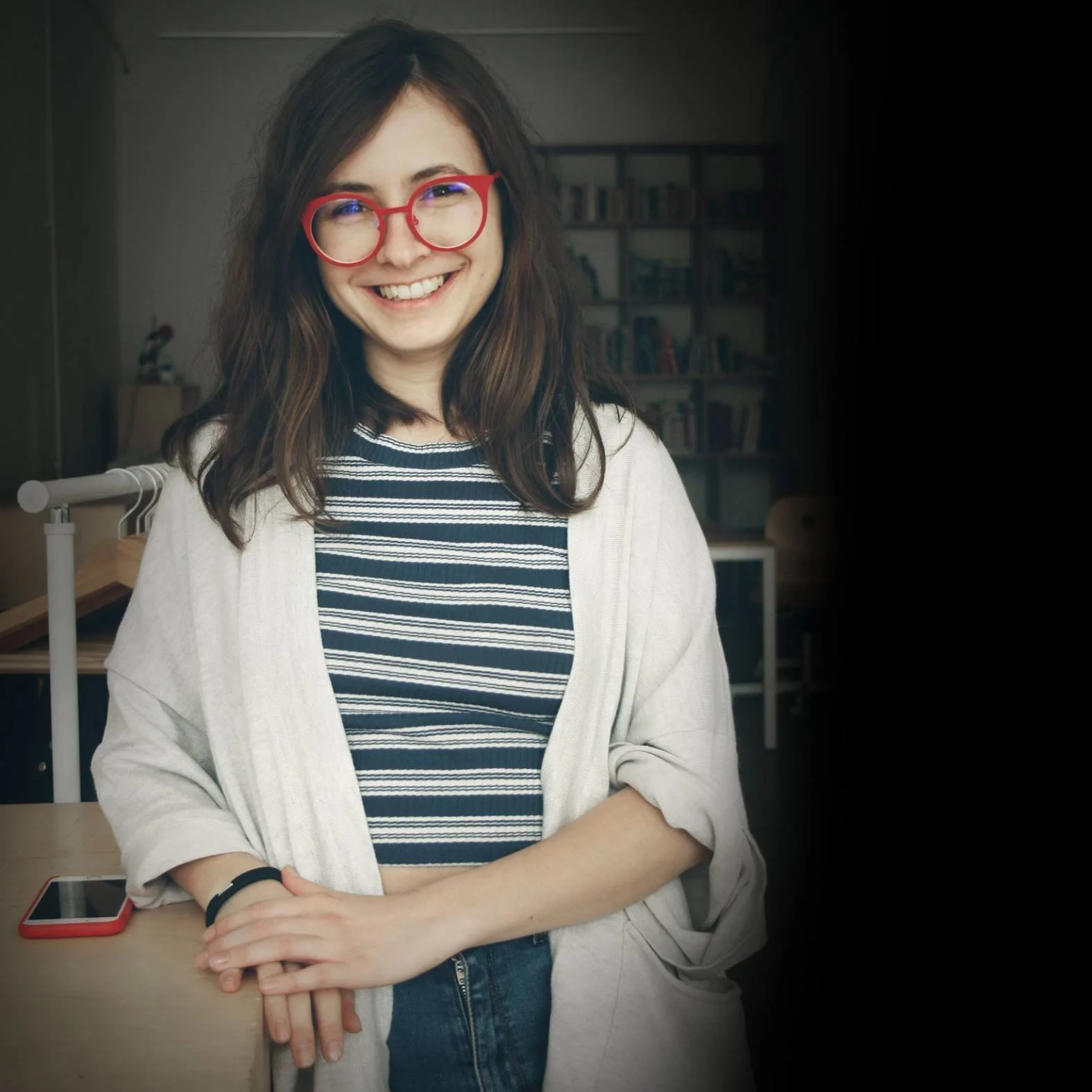 În imagine o vedem pe Iris Popescu care stă în fața bibliotecii de la Firul Ierbii. Ea poartă ochelari și zâmbește larg către cameră