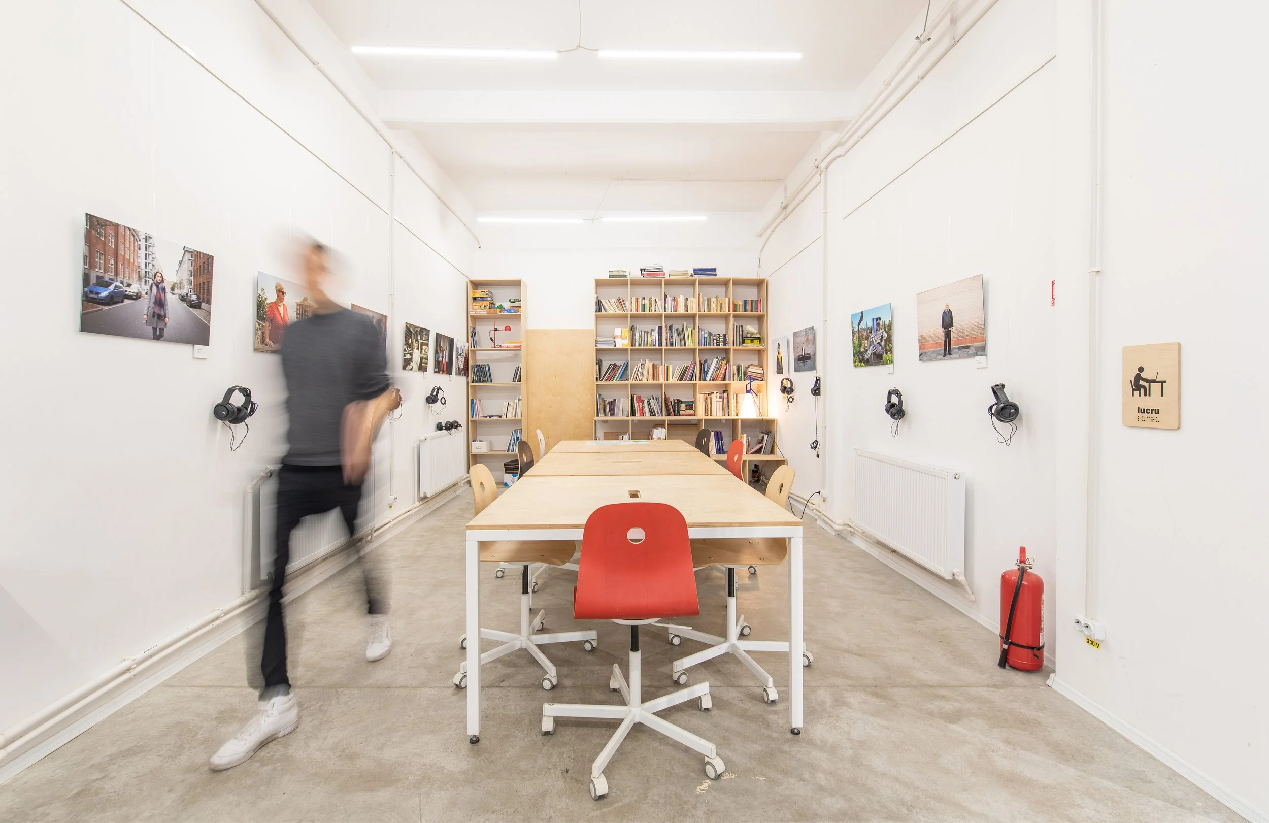 Poza este făcută în biblioteca de La Firul Ierbii. Pe pereți sunt pozele de la o expoziție, fiecare poză cu câte o pereche de căști atașate. În mijloc o masă mare și un băiat surprins în mișcare